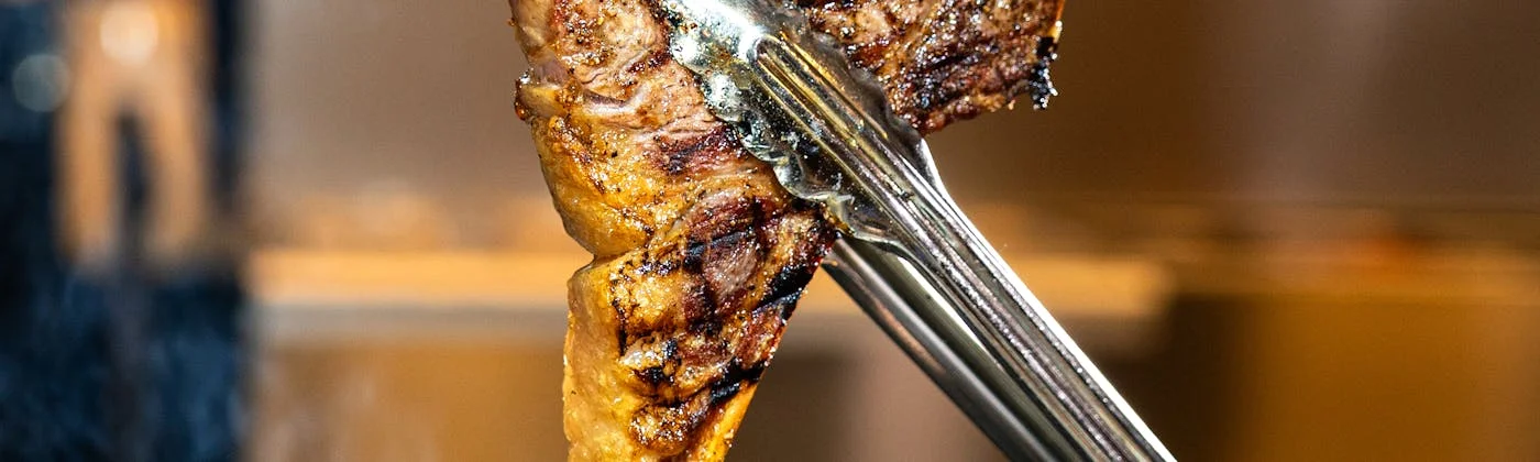 Steak grelhado sendo segurado por um pegador com marcas de grelha visíveis
