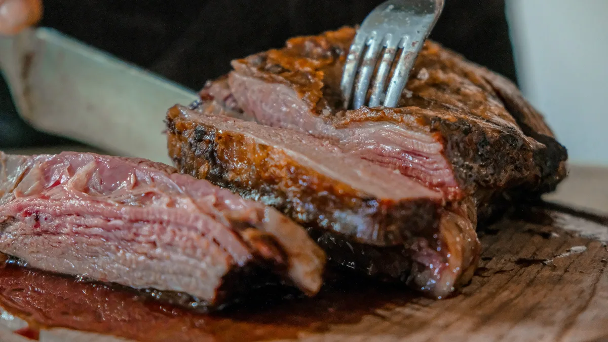 Faca e garfo fatiando carne assada sobre tábua de madeira