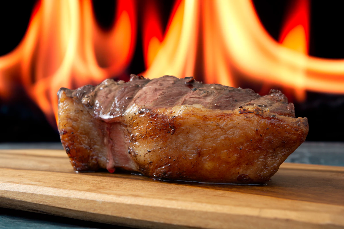 Picanha brasileira com capa de gordura grelhada sobre tábua de madeira, apresentada pronta para fatiar em churrasco